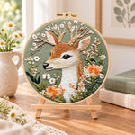 Deer and wild daisies embroidery kit finished hoop displayed on a wooden stand as cozy tabletop decor