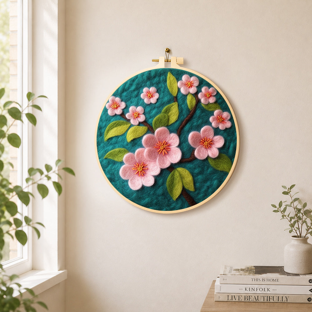 Delicate pink flowers on dark green needle felt wall art displayed in a bright home interior