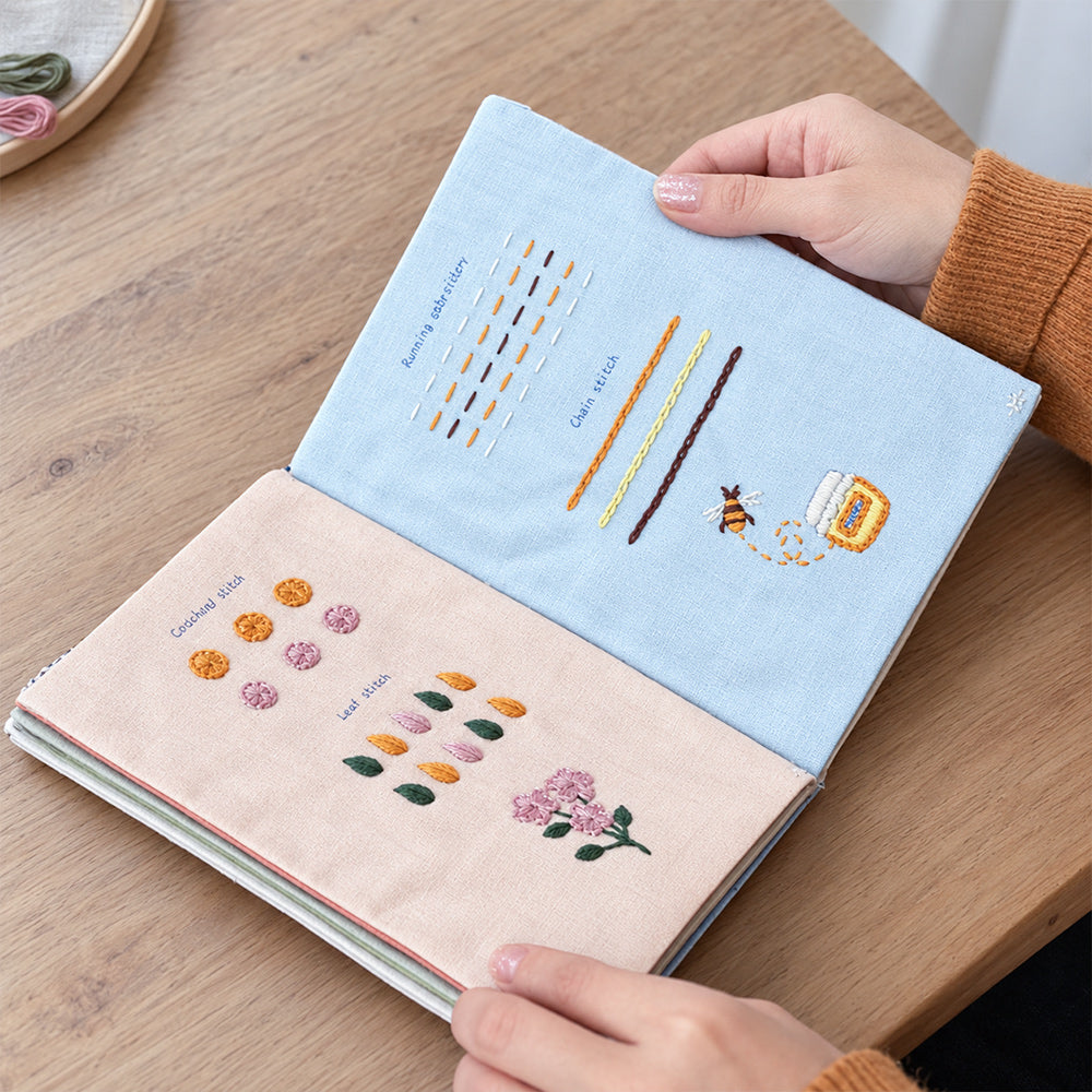 Embroidery stitch practice book displaying a bee, honey jar, floral patterns and beginner stitching exercises