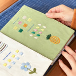 Open embroidery practice book featuring a pineapple, flower designs and decorative stitch samples