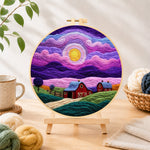 Finished dreamy swirling purple sky and red barn needle felting displayed on a wooden easel