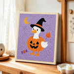 Duck in pumpkin witch outfit punch needle artwork displayed on a table