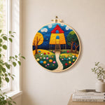 Fairy tale tall red roof cottage needle felt wall art displayed in a bright home interior