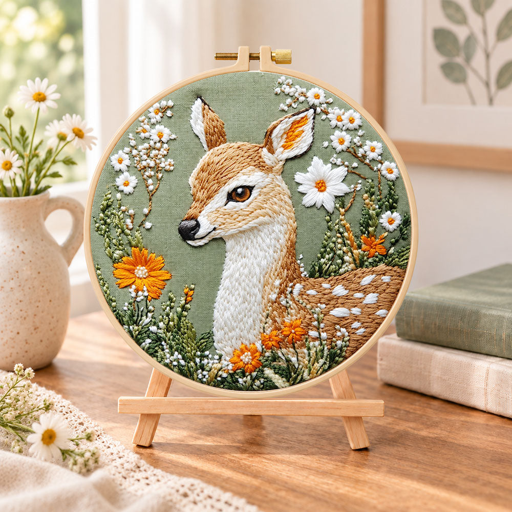 Fawn with daisies and orange blooms embroidery kit finished hoop displayed on a wooden stand as cozy tabletop decor