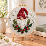 Festive gnome portrait embroidery kit finished hoop displayed on a wooden stand as cozy tabletop decor