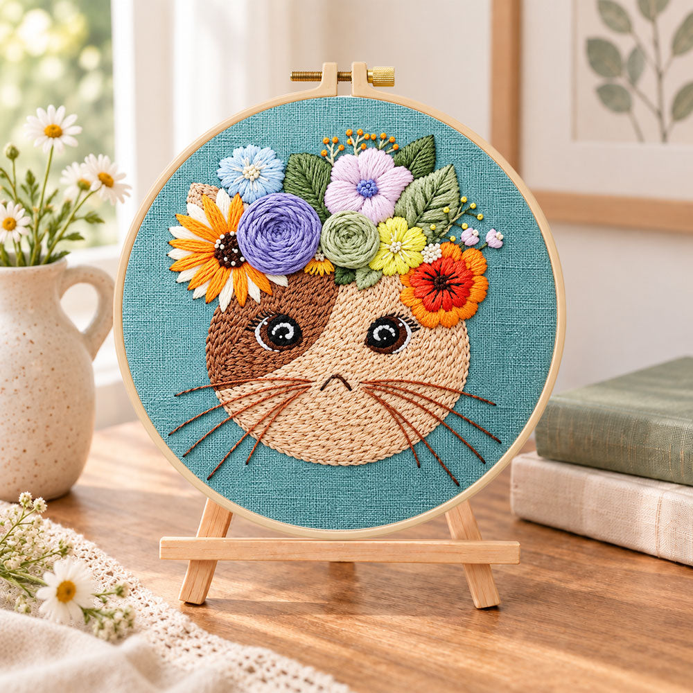 Floral crown kitty embroidery kit finished hoop displayed on a wooden stand as cozy tabletop decor