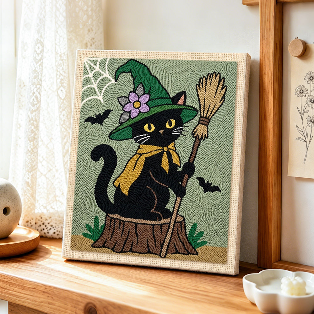 Floral‑hat witch cat with broom punch needle artwork displayed on a table