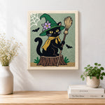 Finished floral‑hat witch cat with broom artwork displayed on a wall