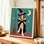 Floral‑hat witch reading book punch needle artwork displayed on a table