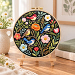 Forest birds and spring blooms embroidery kit finished hoop displayed on a wooden stand as cozy tabletop decor