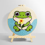 Frog holding a flower punch needle kit for beginners
