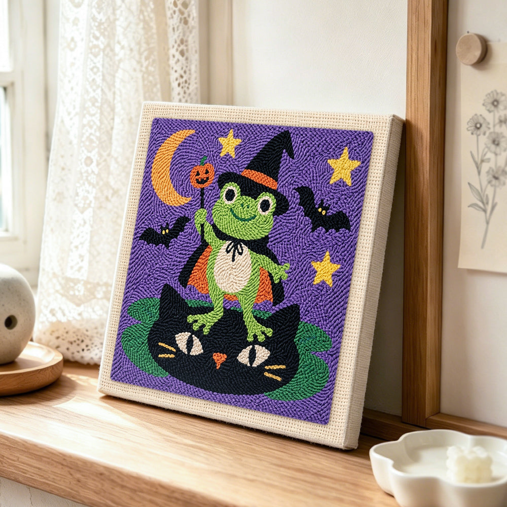 Frog wizard standing on cat punch needle artwork displayed on a table