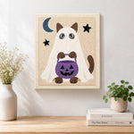 Finished ghost cat holding pumpkin treat bucket artwork displayed on a wall