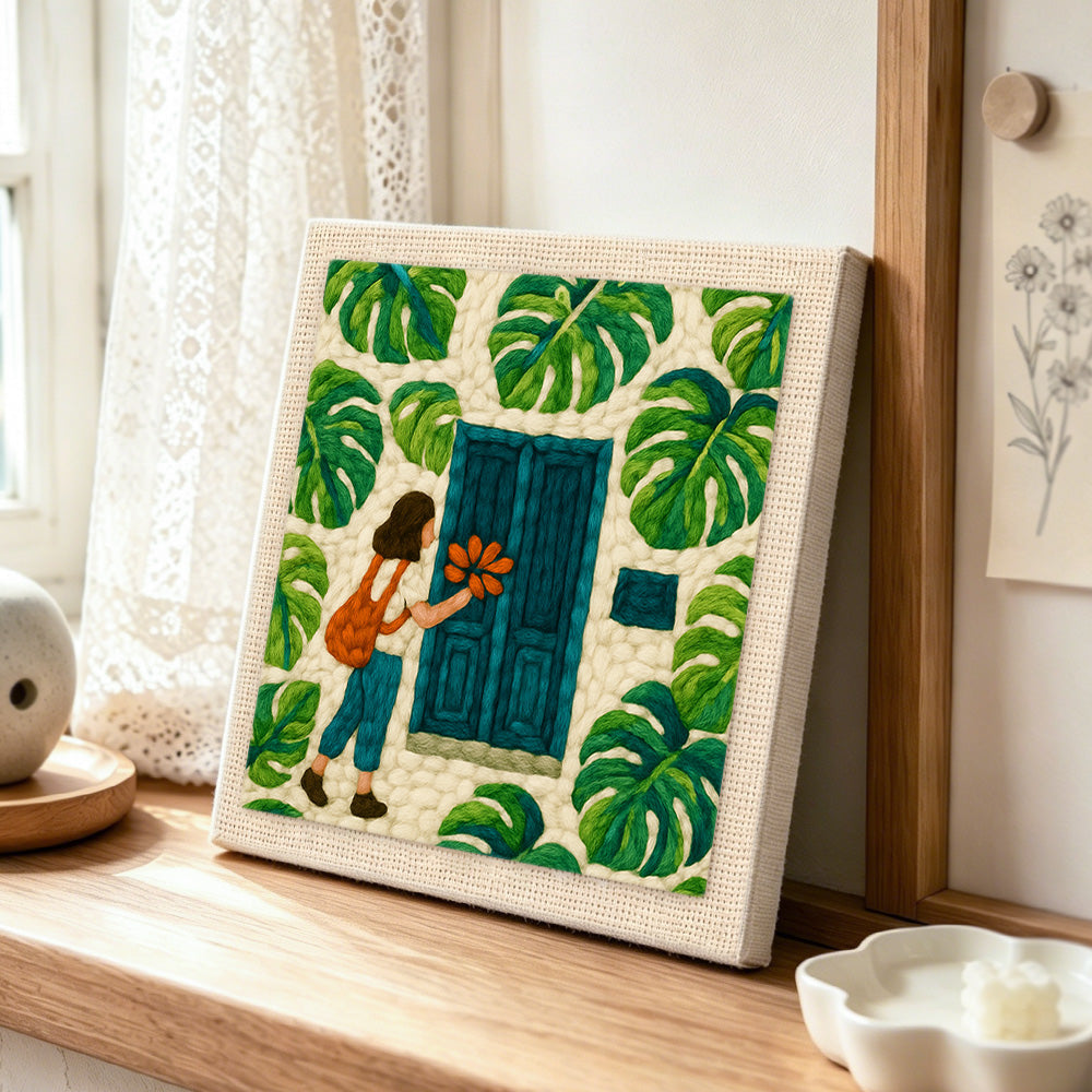 Girl, teal door and monstera leaves punch needle artwork displayed on a table