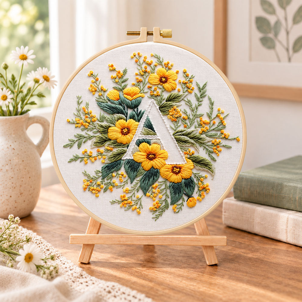 Golden florals and letter a embroidery kit finished hoop displayed on a wooden stand as cozy tabletop decor