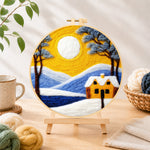 Finished golden sun and blue mountain snowscape needle felting displayed on a wooden easel
