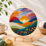 Finished gradient clouds, bright yellow sunset and colorful hills needle felting displayed on a wooden easel