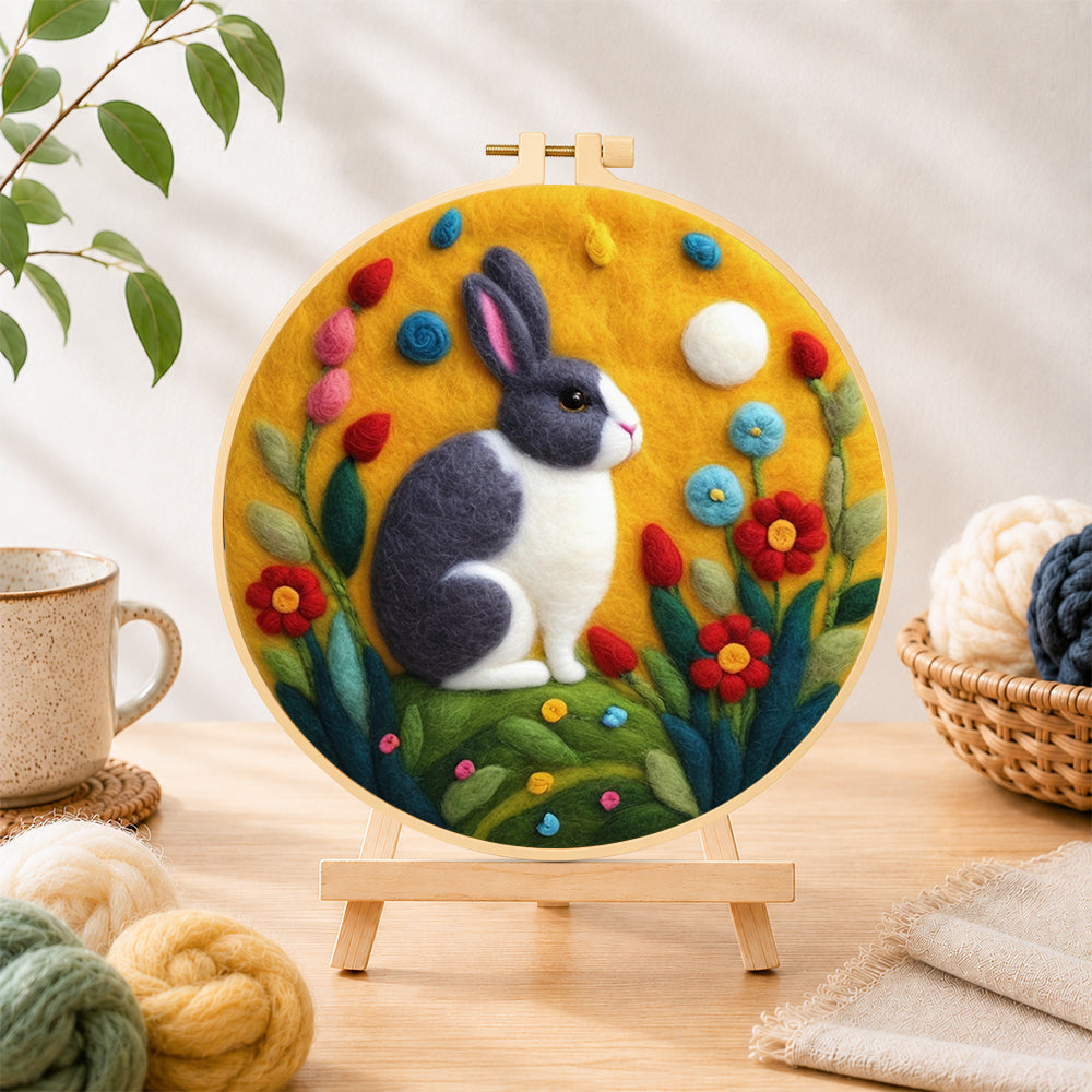 Finished gray and white rabbit among flowers needle felting displayed on a wooden easel
