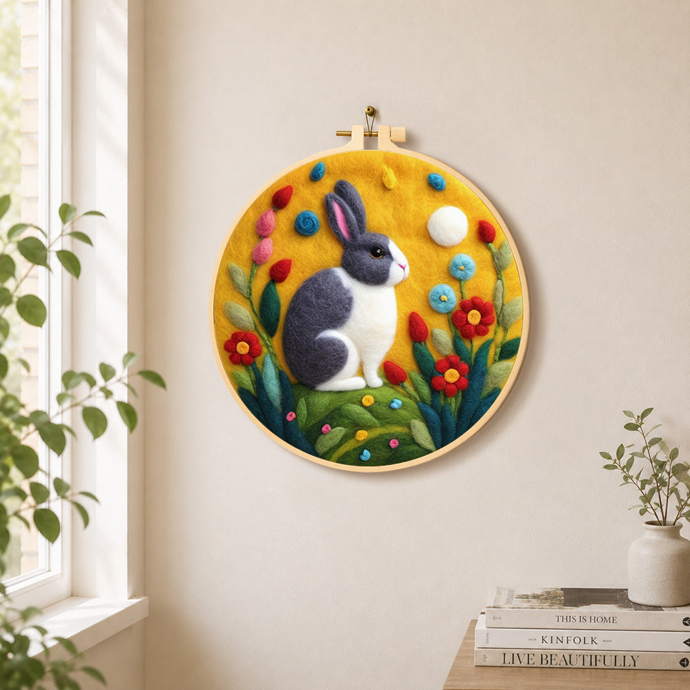 Gray and white rabbit among flowers needle felt wall art displayed in a bright home interior