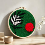 Green botanical with red sun punch needle artwork displayed on a table