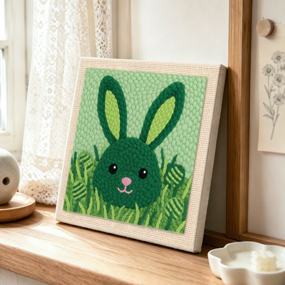 Green bunny hiding in grass punch needle artwork displayed on a table