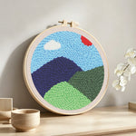 Green mountains in spring punch needle artwork displayed on a table