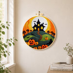 Haunted house on hill with pumpkins needle felt wall art displayed in a bright home interior