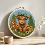 Highland cow and mushrooms on the green grass punch needle artwork displayed on a table