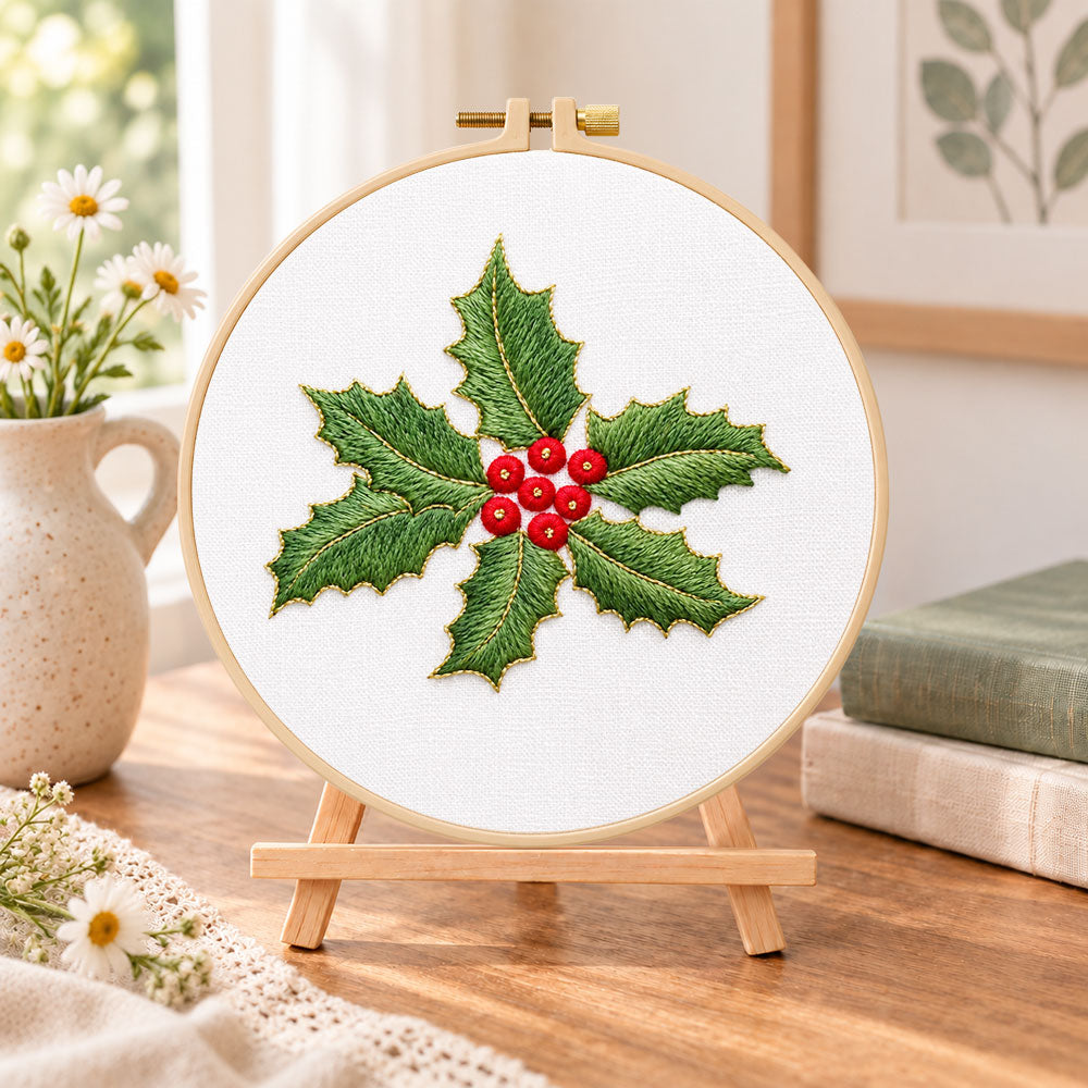 Holly leaves and berries embroidery kit finished hoop displayed on a wooden stand as cozy tabletop decor