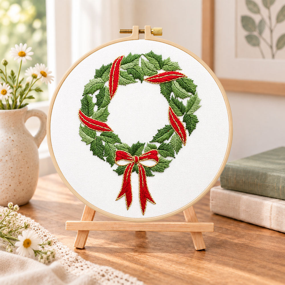 Holly wreath with bow embroidery kit finished hoop displayed on a wooden stand as cozy tabletop decor