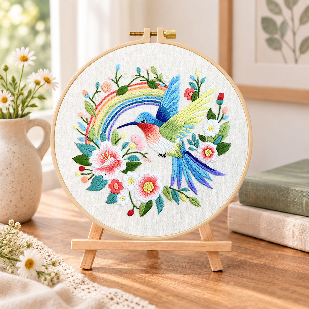 Hummingbird with rainbow embroidery kit finished hoop displayed on a wooden stand as cozy tabletop decor