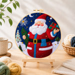Finished jolly santa holding gift and tree needle felting displayed on a wooden easel