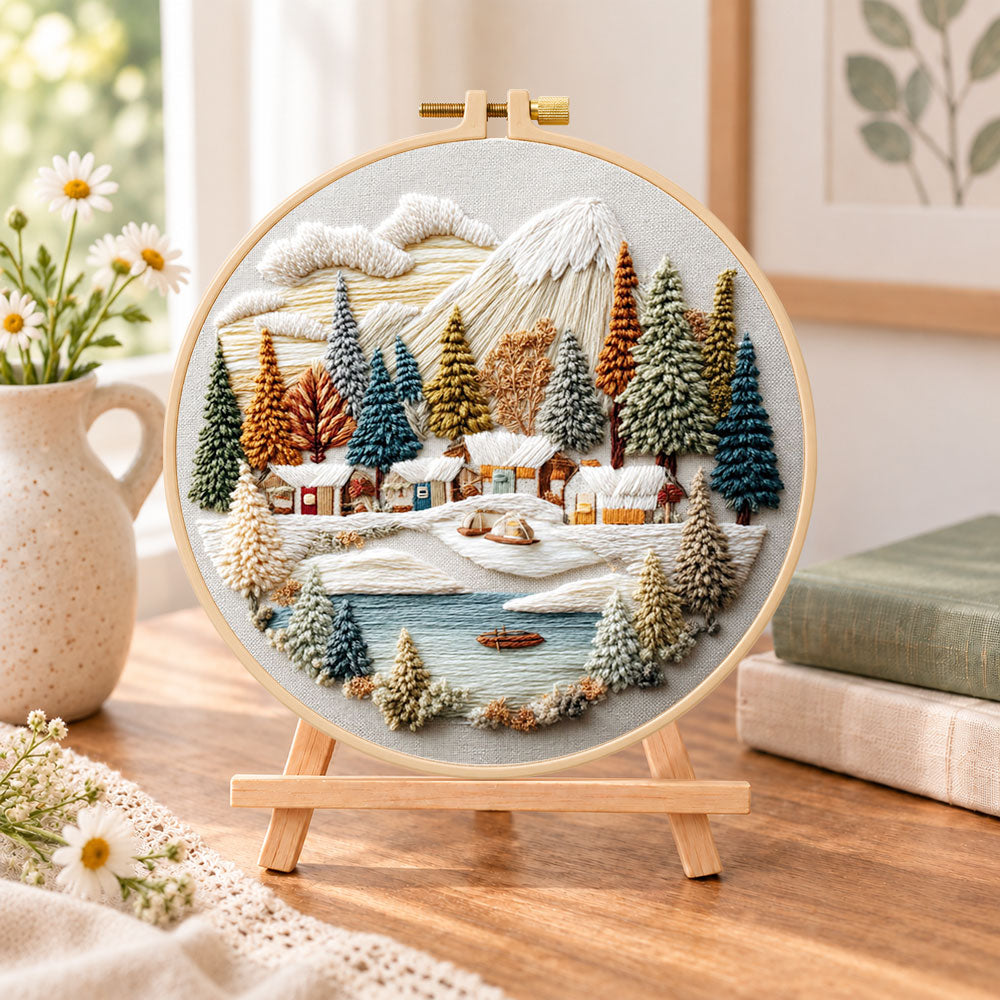 Lakeside snow town embroidery kit finished hoop displayed on a wooden stand as cozy tabletop decor