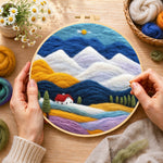 Creating the layered mountains and red-roof cottage wool painting by hand with a felting needle