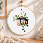 Lazy cat in hanging planter embroidery hoop wall art displayed as warm and cozy handmade home decor