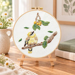 Little bird looking at loquat fruits embroidery kit finished hoop displayed on a wooden stand as cozy tabletop decor