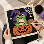 Creating handmade little witch frog sitting on pumpkin punch needle artwork
