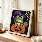 Little witch frog sitting on pumpkin punch needle artwork displayed on a table