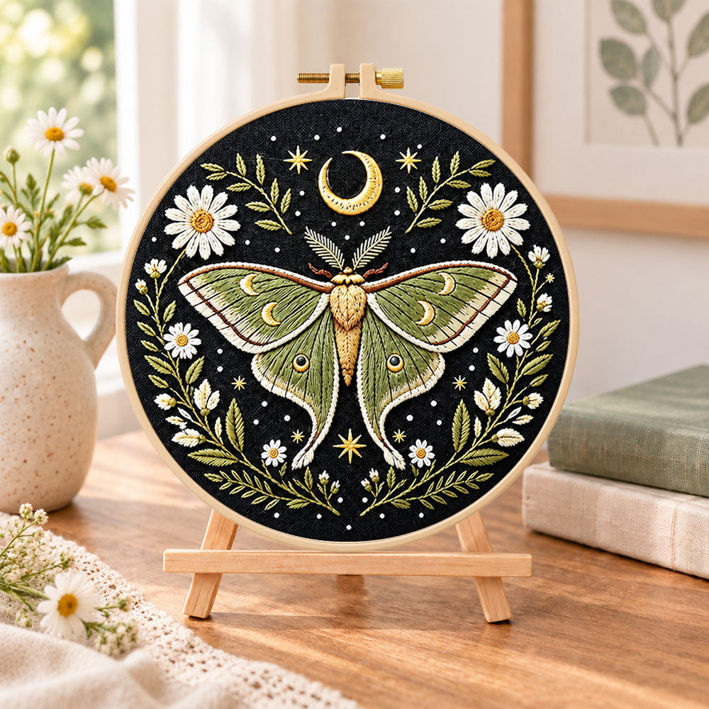 Luna moth and crescent moon embroidery kit finished hoop displayed on a wooden stand as cozy tabletop decor