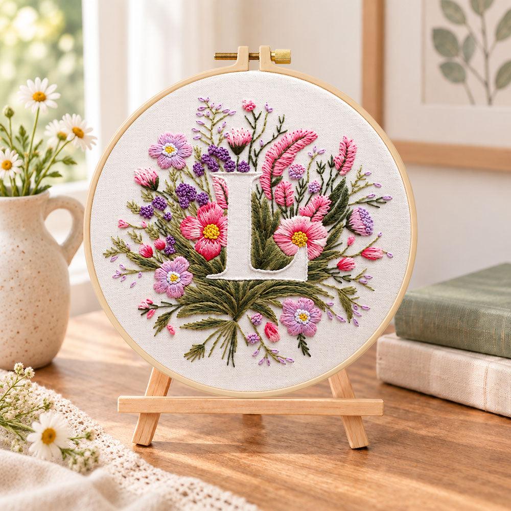 Mauve wildflowers and letter l embroidery kit finished hoop displayed on a wooden stand as cozy tabletop decor