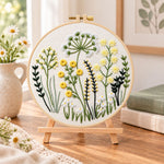 Meadow herbs hand embroidery kit finished hoop displayed on a wooden stand as cozy tabletop decor
