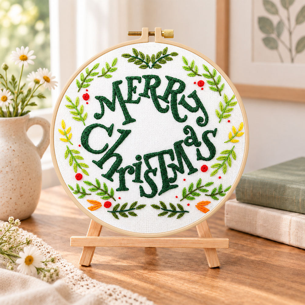 Merry christmas wreath embroidery kit finished hoop displayed on a wooden stand as cozy tabletop decor