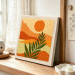 Minimalist leaf and mountain scenery punch needle artwork displayed on a table