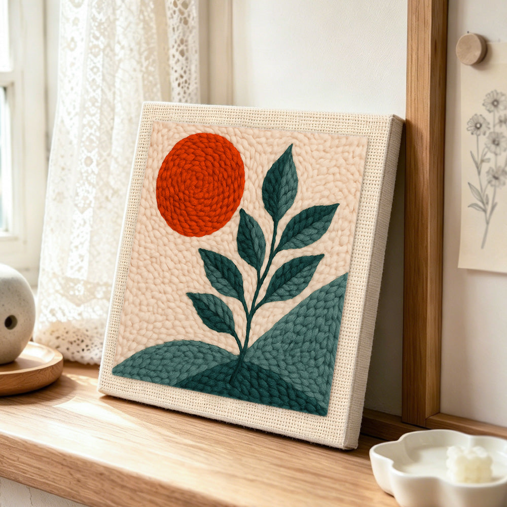 Minimalist sun and plant punch needle artwork displayed on a table