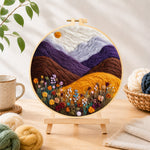 Finished misty purple mountains and wildflowers needle felting displayed on a wooden easel