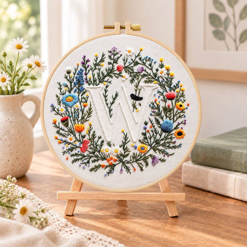 Mixed floral wreath and letter w embroidery kit finished hoop displayed on a wooden stand as cozy tabletop decor