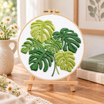 Monstera leaf embroidery kit finished hoop displayed on a wooden stand as cozy tabletop decor