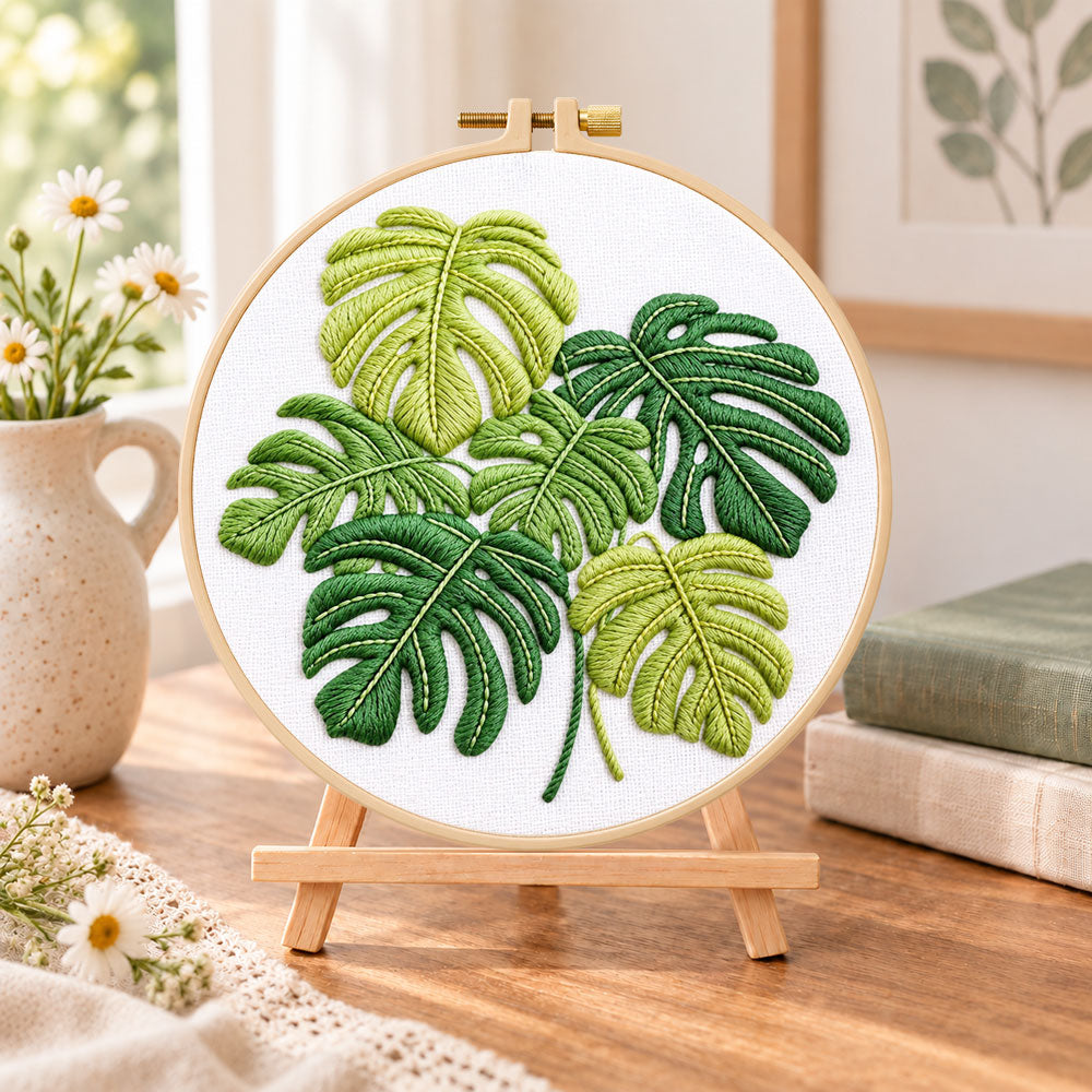 Monstera leaf embroidery kit finished hoop displayed on a wooden stand as cozy tabletop decor