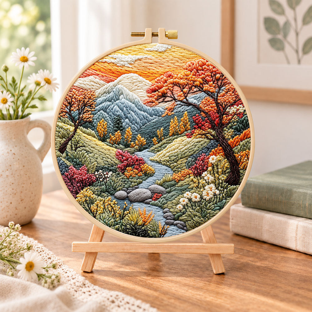 Mountain stream at sunset embroidery kit finished hoop displayed on a wooden stand as cozy tabletop decor