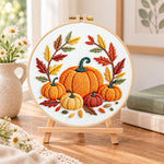 Multiple pumpkins with autumn leaves embroidery kit finished hoop displayed on a wooden stand as cozy tabletop decor
